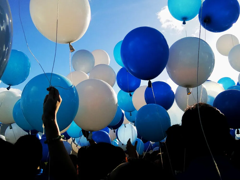 Crowd of people holding blue and white balloons up to the blue sky