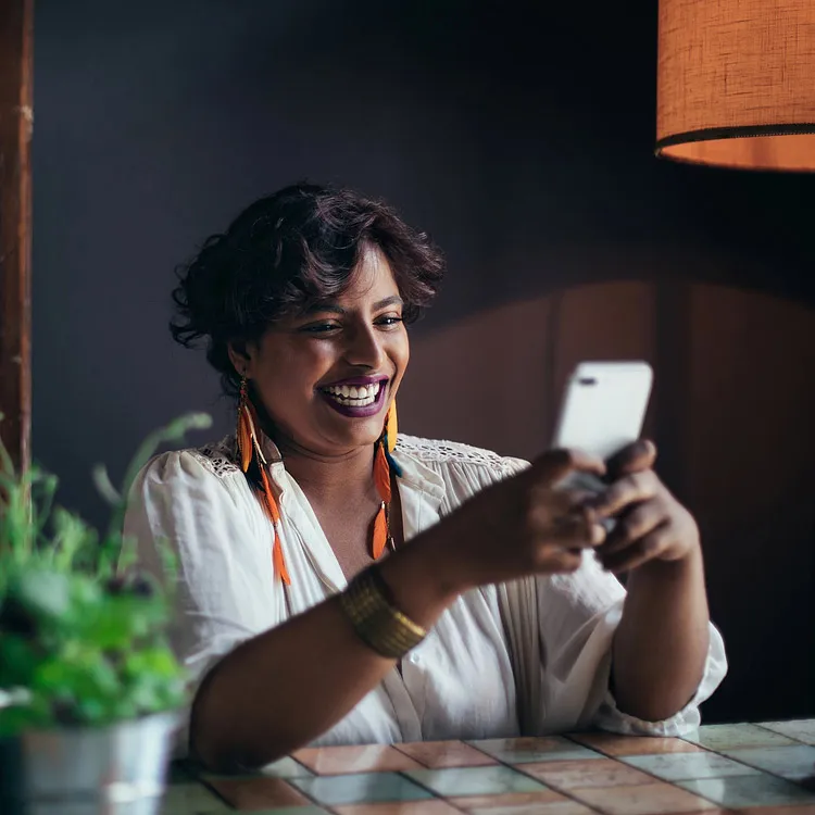 Indian woman at her desk smiling while using her phone