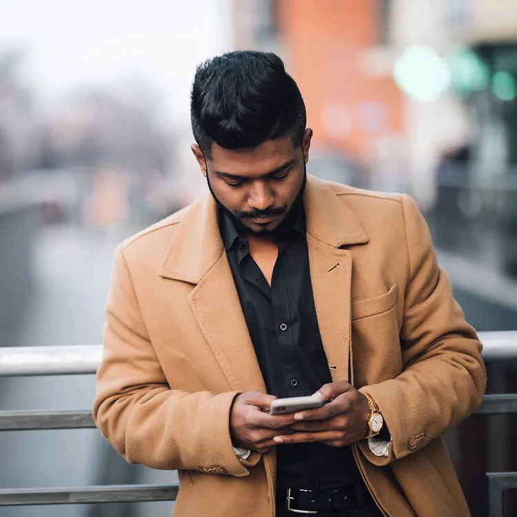A man leaning up against a railing looking down at his cell phone