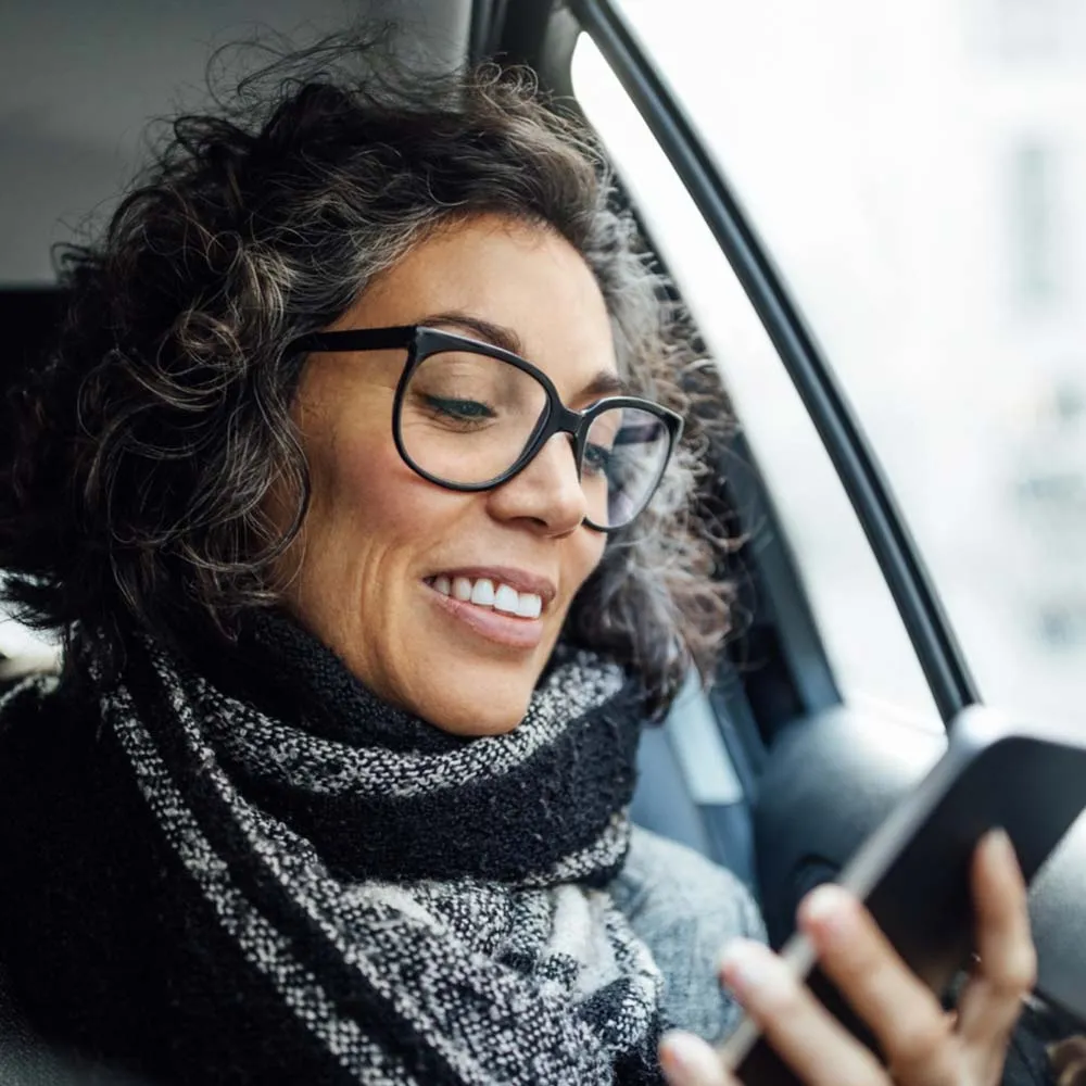 A woman sitting in her car smiling while looking down at her phone