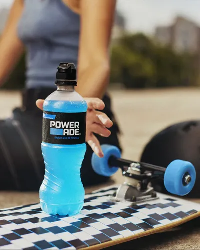 A woman grabbing her powerade drink that's sitting on top of a skateboard