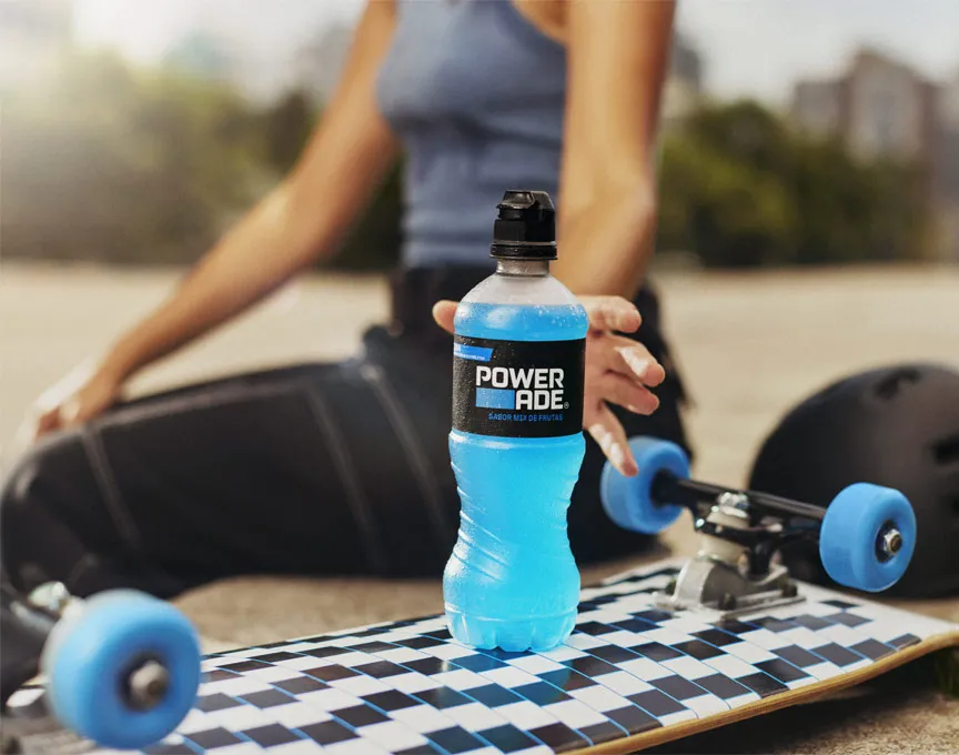 Uma mulher pegando uma bebida Powerade que está em cima de um skate
