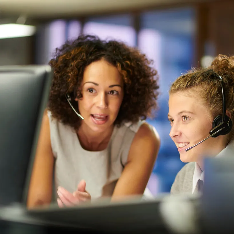 Dua wanita memakai headset mengamati monitor komputer di depannya