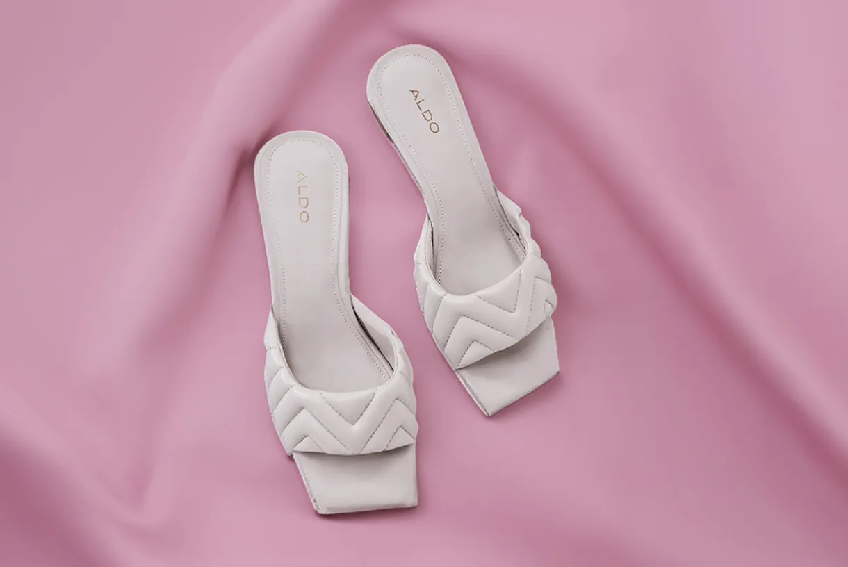 Un par de zapatos de vestir blancos sobre un fondo rosa.