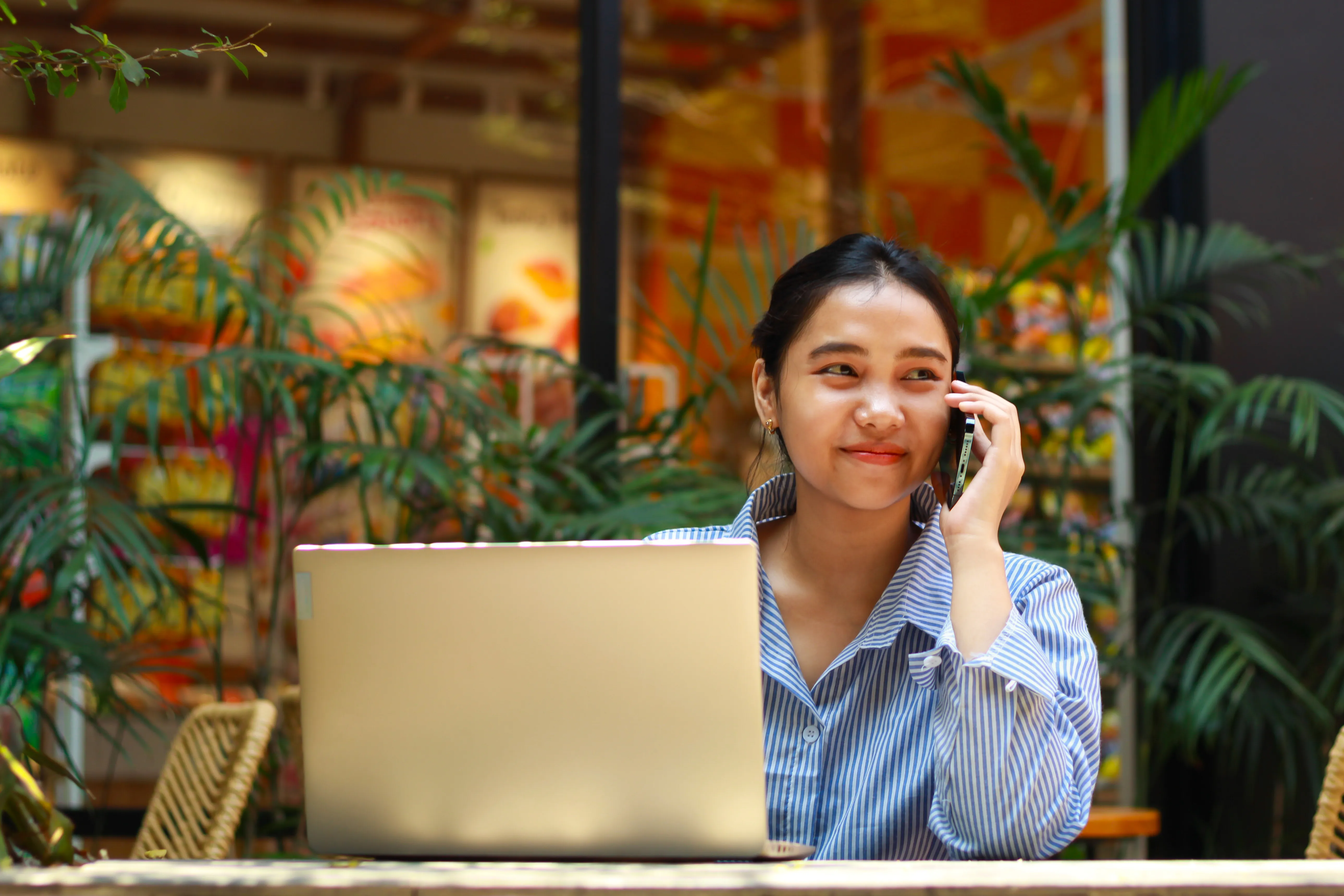 A woman talking on her phone while using her laptop.